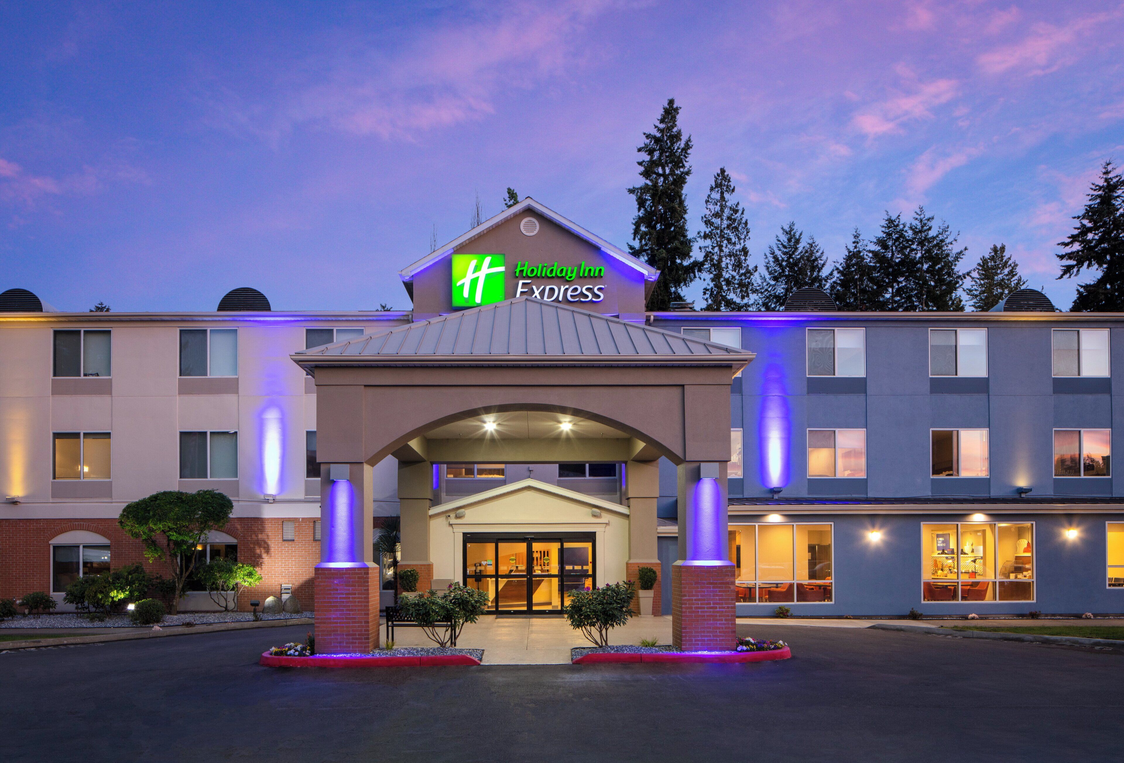 Ein Holiday Inn Express Gebäude mit auffälliger Beschilderung, einem überdachten Eingang und einem Parkplatz.