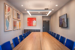 A conference room with a long wooden table, blue chairs, and framed artwork on the walls.