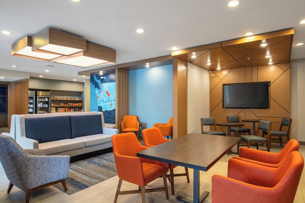 A modern hotel lobby with a seating area, a television, and a snack bar.