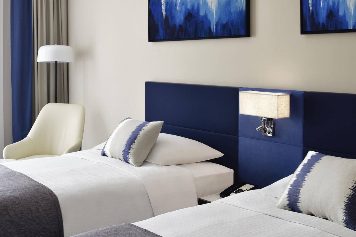 Habitación de hotel con dos camas, un escritorio, una silla y obras de arte en las paredes.