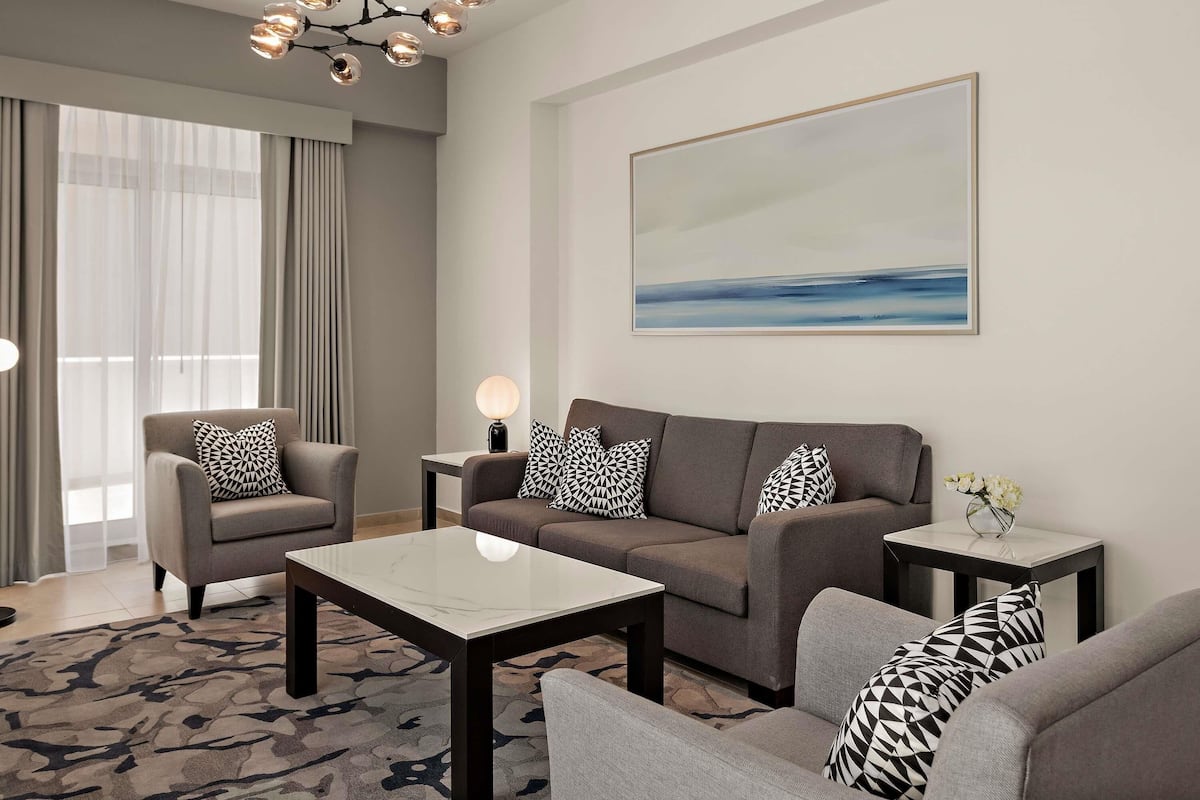Una sala de estar moderna con un sofá, sillones, una mesa de centro, una mesita auxiliar, una lámpara de pie y un cuadro en la pared.