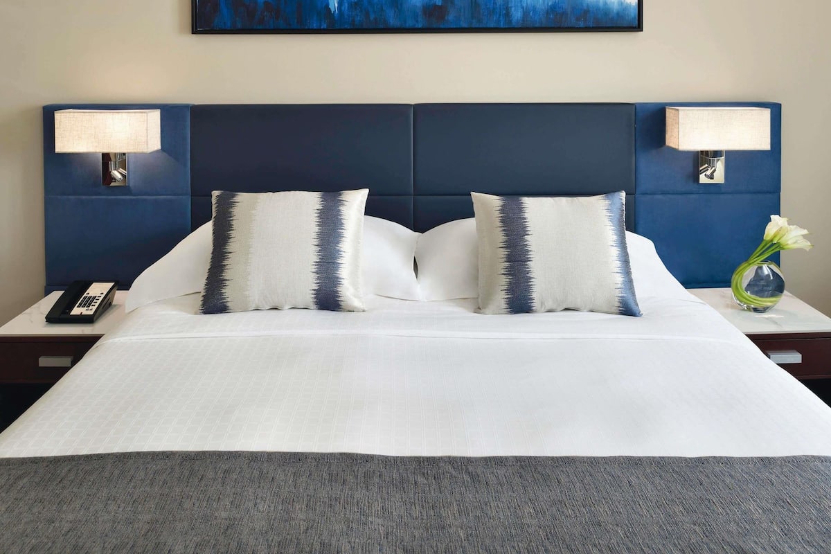 A hotel room with a large bed, two bedside lamps, a phone on the nightstand, and a painting on the wall.