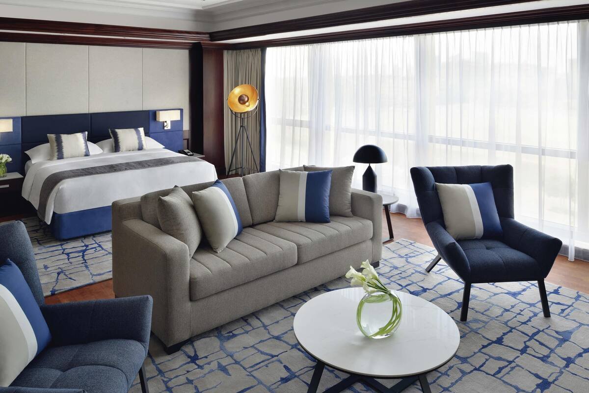 Una habitación de hotel con cama, sofá, sillón y una mesa redonda con un florero.