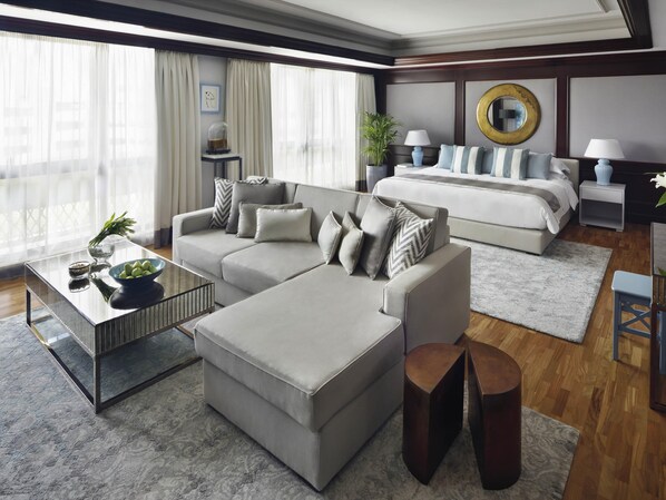 A modern hotel room with a sofa, ottoman, a small table with a bowl of fruit, a bed, a nightstand, and a large window with curtains. - Mövenpick Hotel & Apartments Bur Dubai (Dubai)