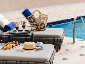 Zona relax a bordo piscina con tavolo, cesto e vista sulla piscina.