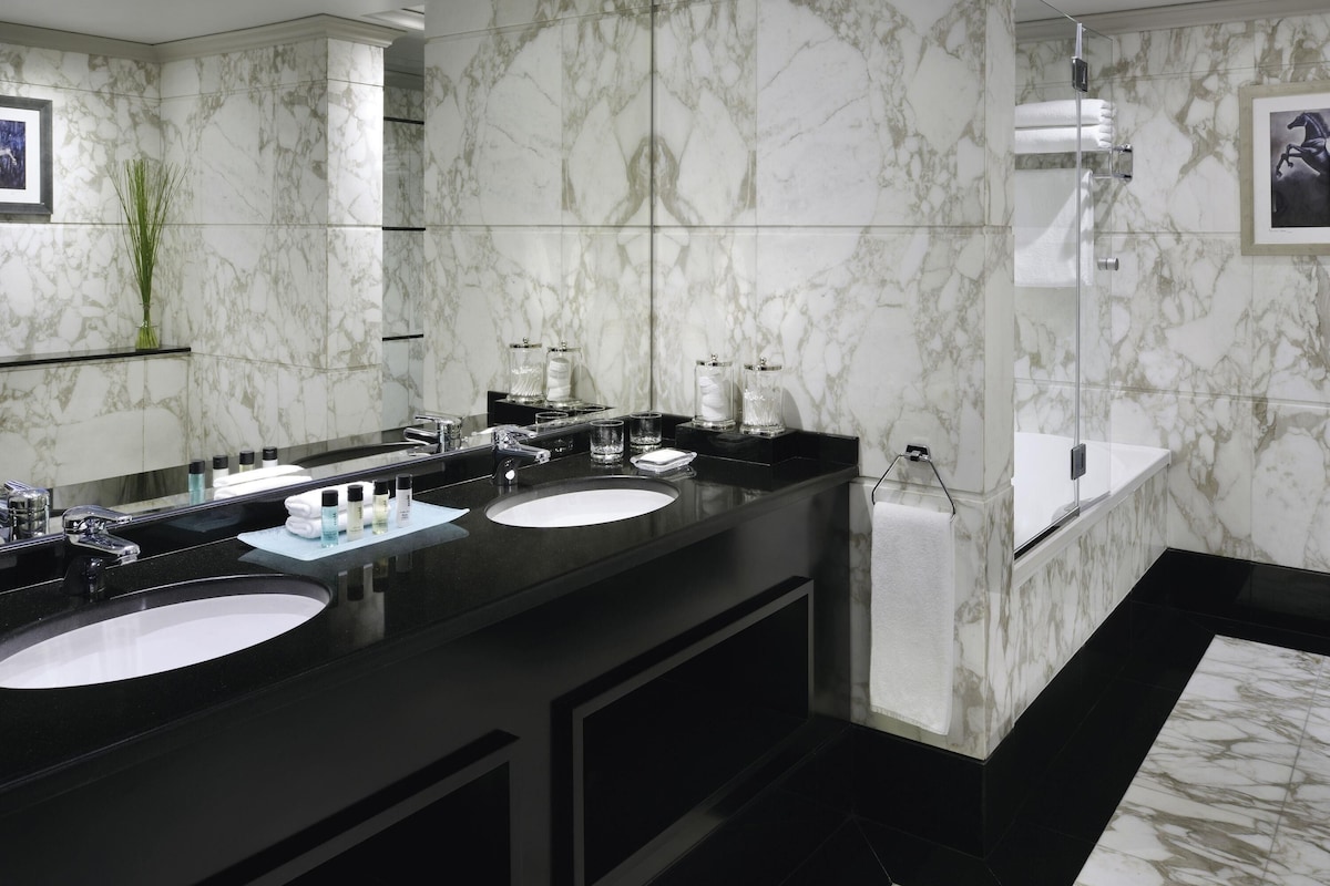 Un baño moderno con dos lavamanos, paredes de mármol y cabina de ducha de vidrio.
