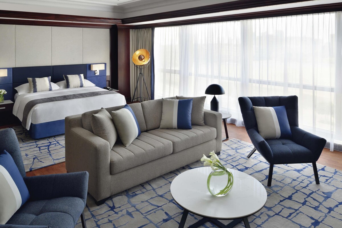 Een hotelkamer met een bed, een bank, een fauteuil en een ronde tafel met een vaas.