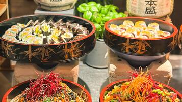 A table with various dishes, including sushi and salads, in decorative bowls.