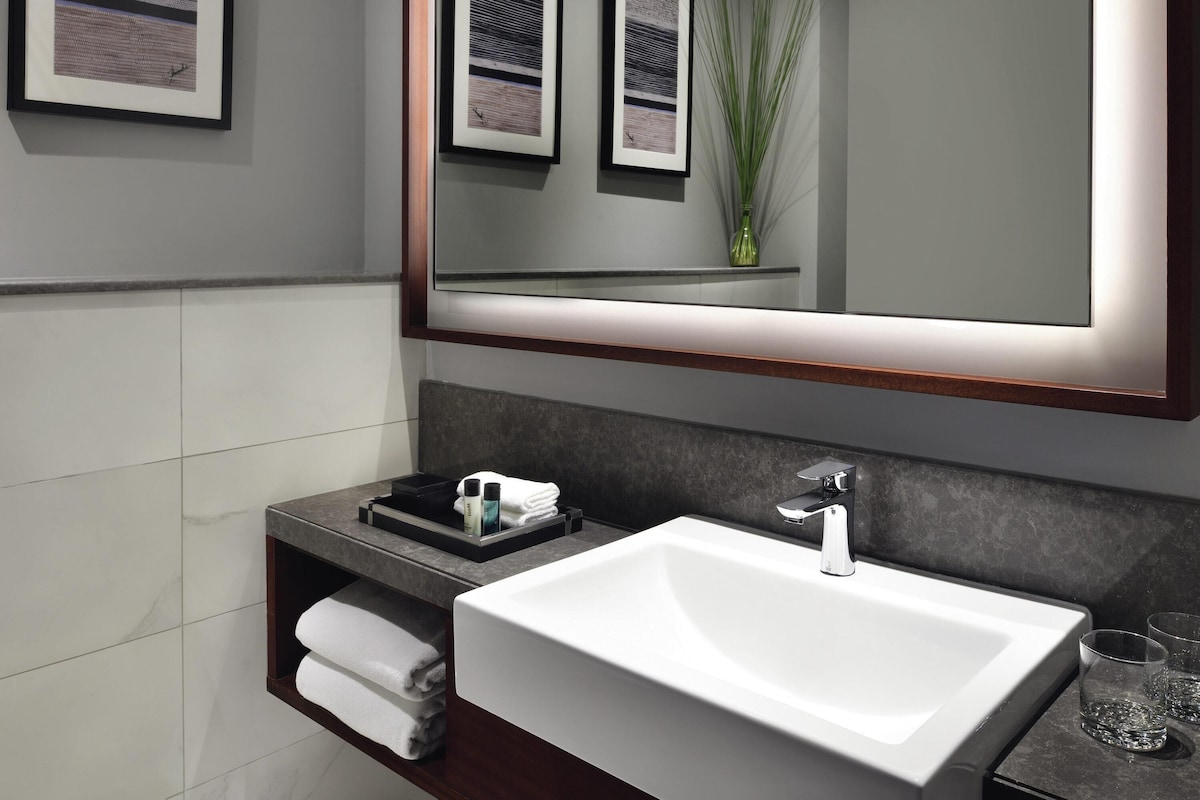 Un baño moderno con un espejo grande, lavamanos blanco y un perchero para toallas.