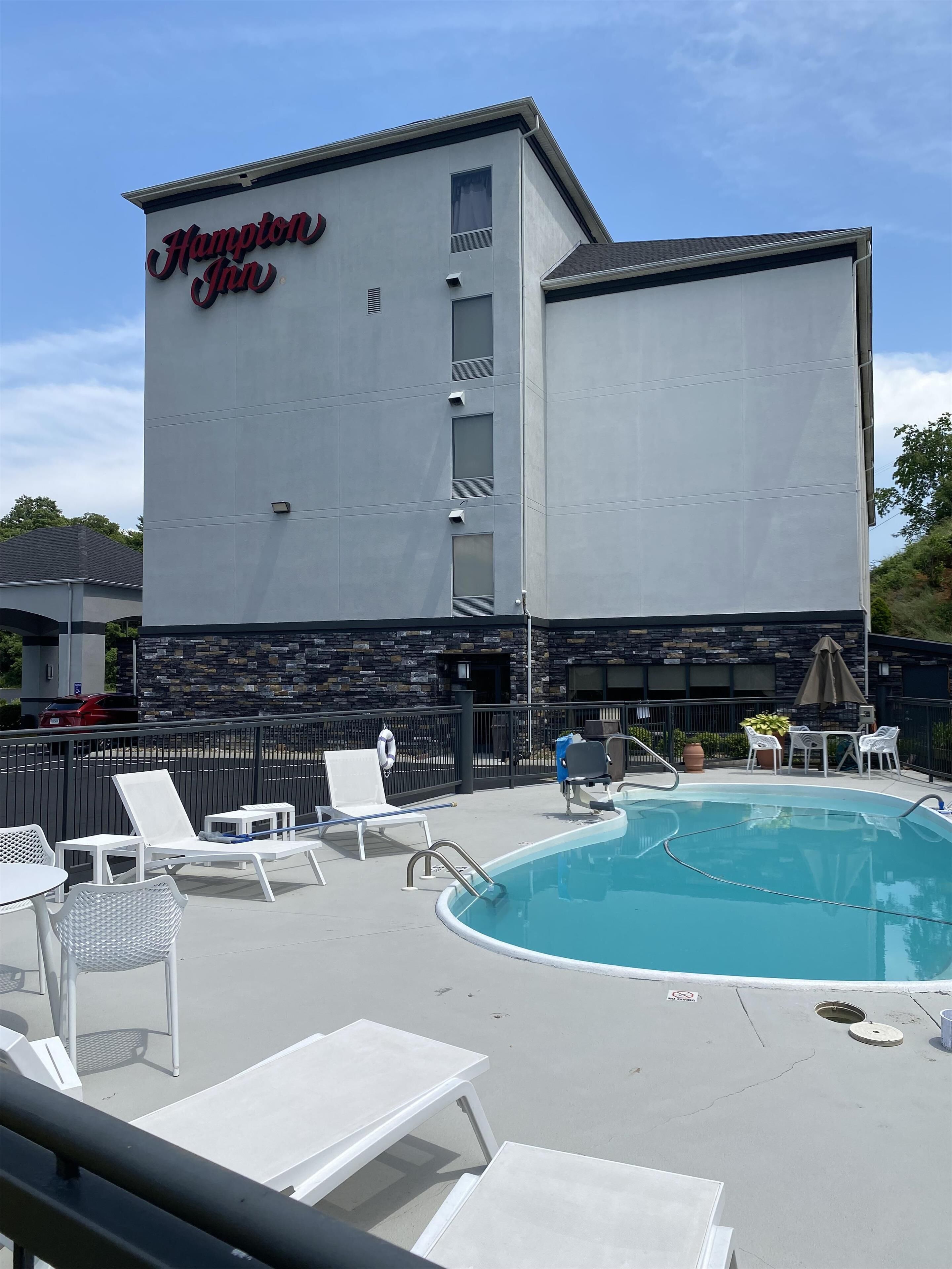 A Hampton Inn building with a swimming pool, outdoor seating, and a stone facade.