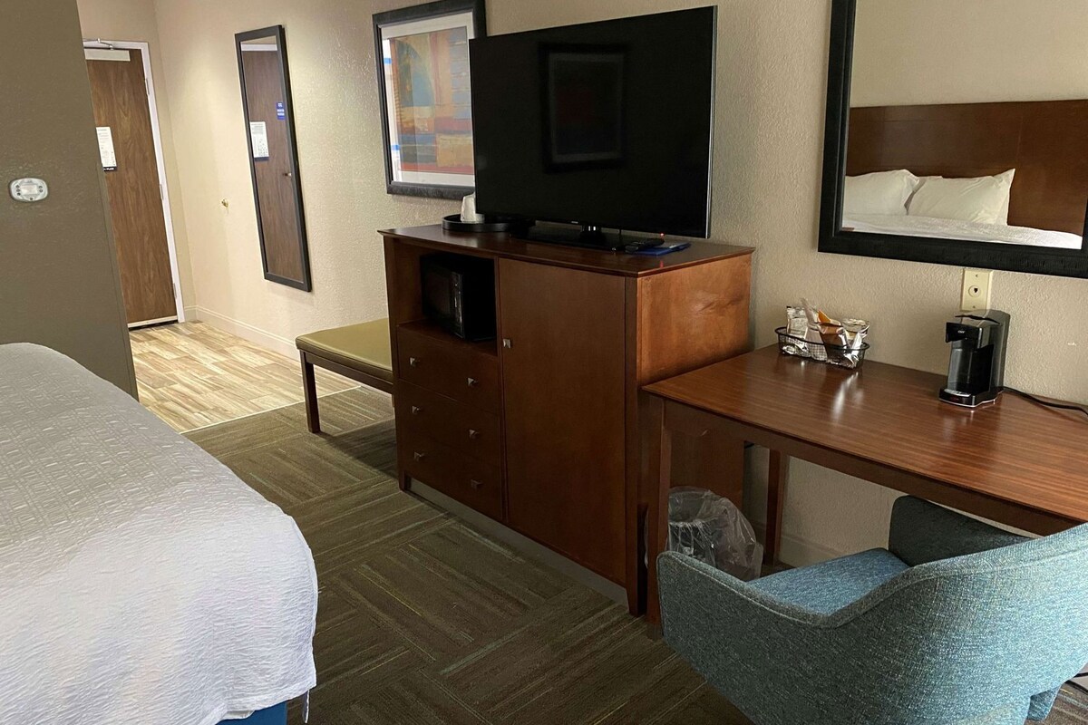 Una habitación de hotel con cama, escritorio con televisor, silla y cafetera.