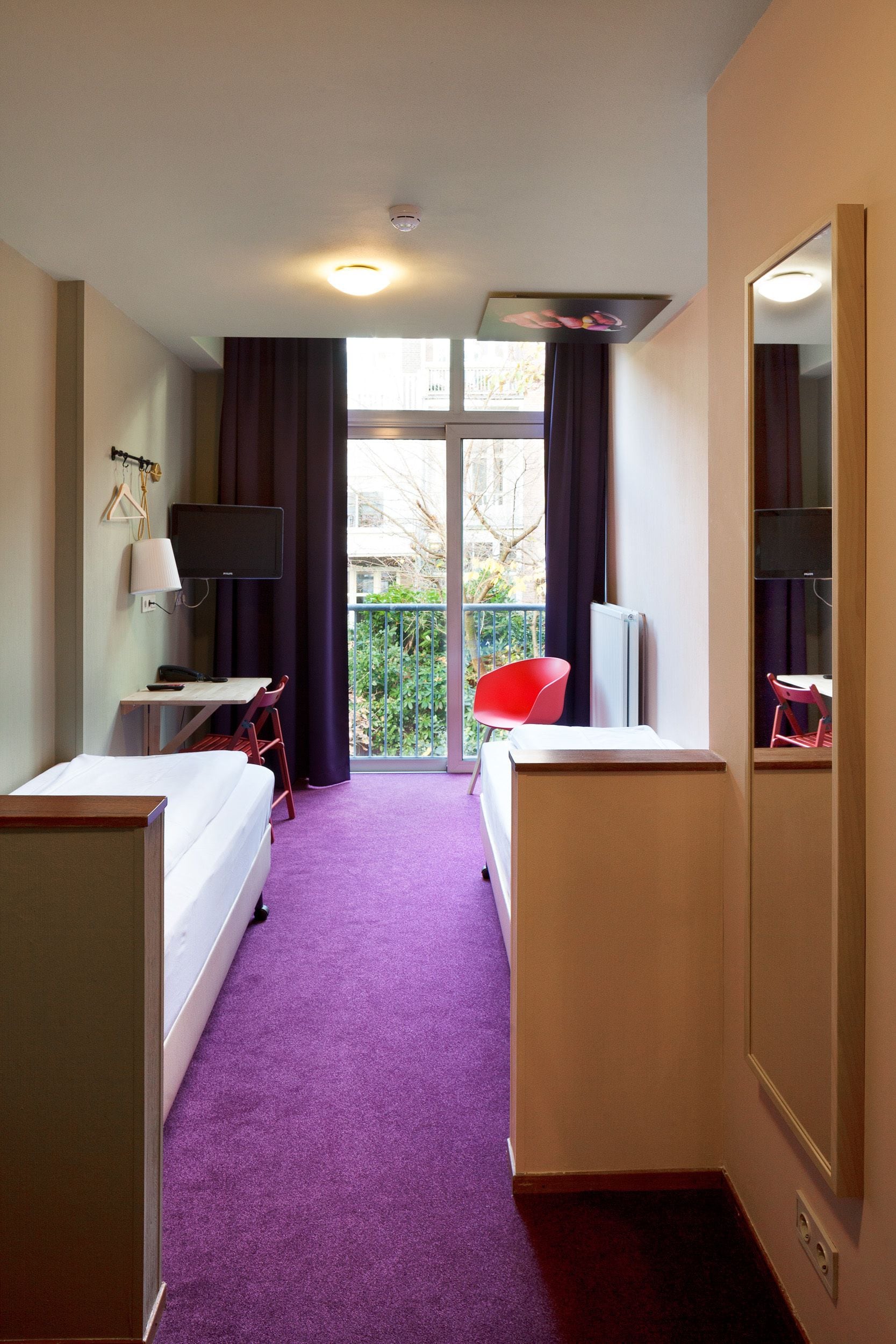 Una habitación de hotel con cama, escritorio, silla y un gran ventanal con cortinas.