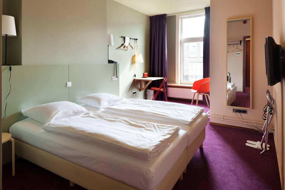 A hotel room with two beds, a desk, a chair, a mirror, and a television.