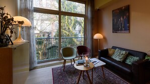 A modern living room with a large window, a sofa, two chairs, a table with a candle, and a painting on the wall. - Hotel The Neighbour's Magnolia (Amsterdam)