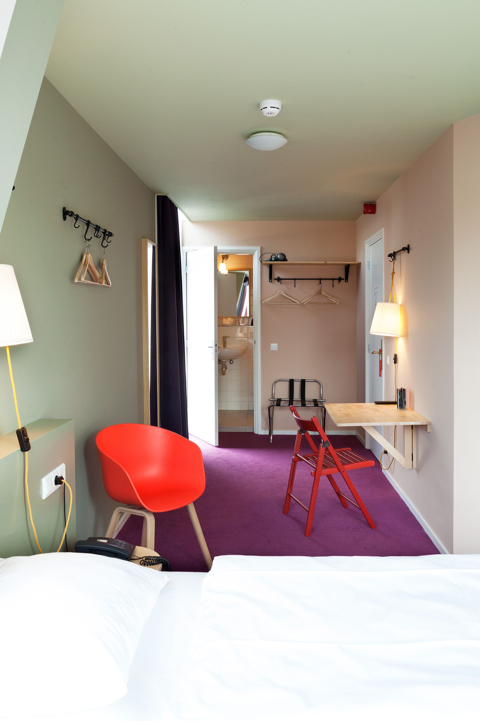 A hotel room with a bed, a desk with a chair, a bathroom, and a coat rack.