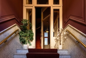 A grand entrance with marble steps, a wooden handrail, and potted plants.