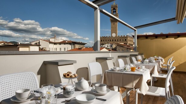 A rooftop dining area with tables set for breakfast, overlooking a historic building with a clock tower.