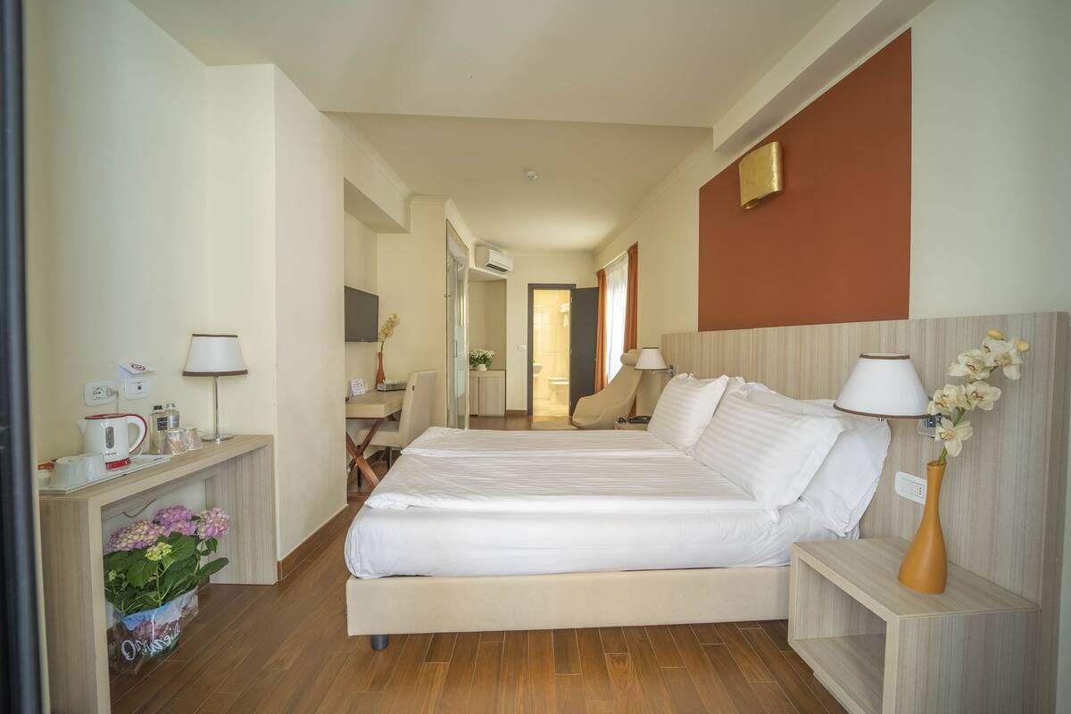 A hotel room with a bed, bedside tables, a desk, and a chair.