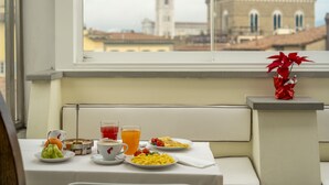 A breakfast table with plates of food, a cup, and a glass of orange juice, set against a window with a view of a historic building.