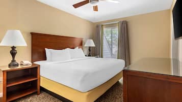 A hotel room with a large bed, two bedside tables with lamps, a ceiling fan, a TV, and a window with curtains.