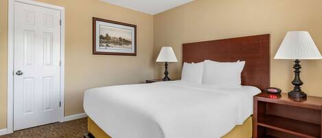 Una habitación de hotel con una cama, dos lámparas de noche, una mesita de noche, un ventilador de techo, un cuadro en la pared y una puerta.