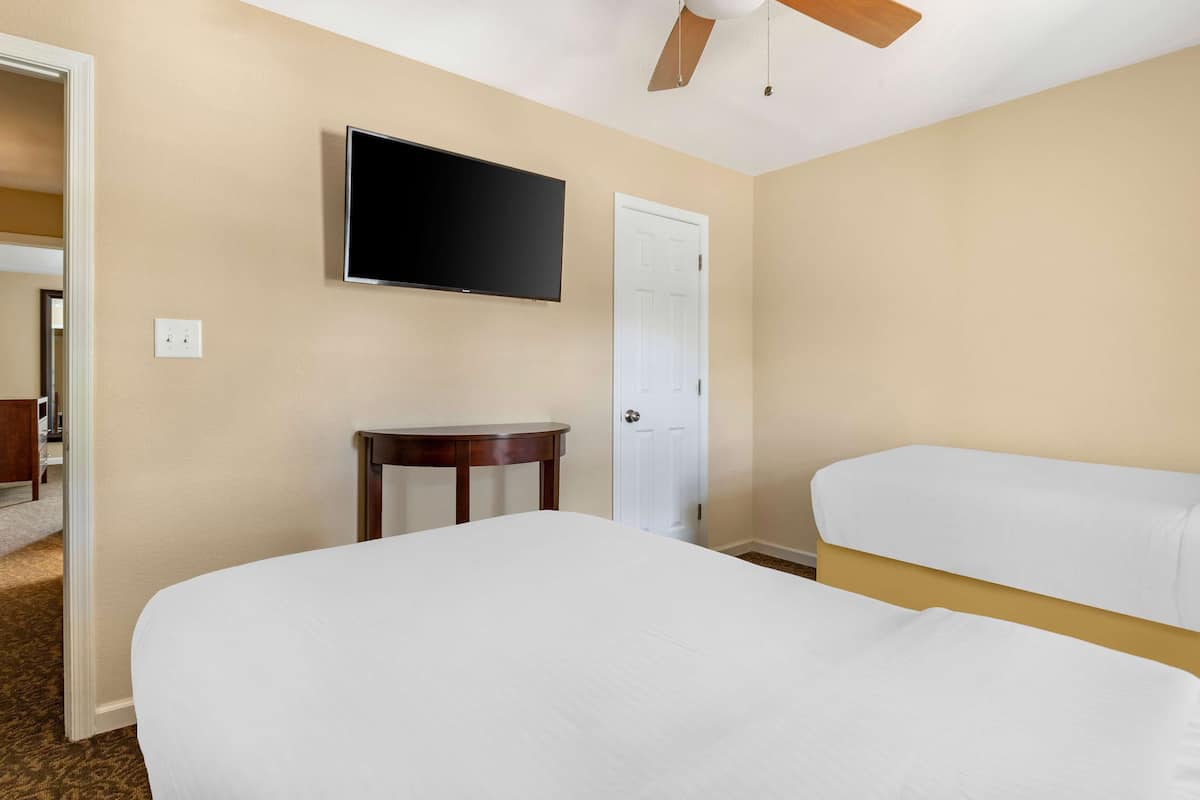 Ein Hotelzimmer mit Bett, Wandfernseher, Tür und kleinem Tisch.