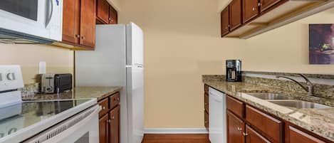 Una cocina con armarios de madera, un refrigerador blanco, un microondas, un tostador y una encimera de granito.