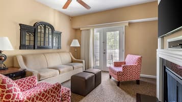 A living room with a beige sofa, patterned armchairs, a fireplace, and a ceiling fan.