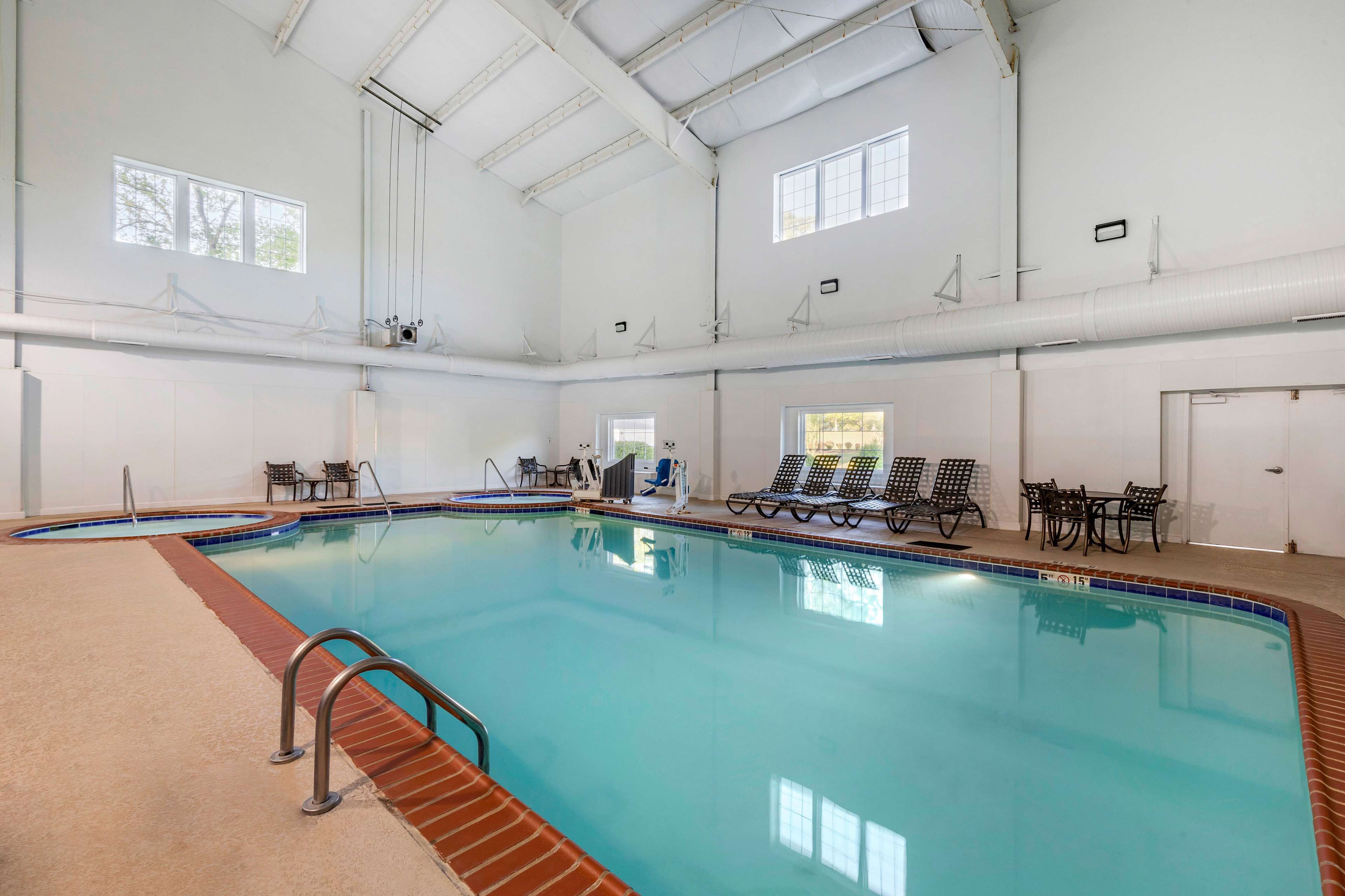Una piscina interior con agua cristalina, rodeada de sillones de descanso y un suelo de baldosas.