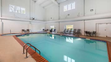 Una piscina interior con agua cristalina, rodeada de sillones de descanso y un suelo de baldosas.