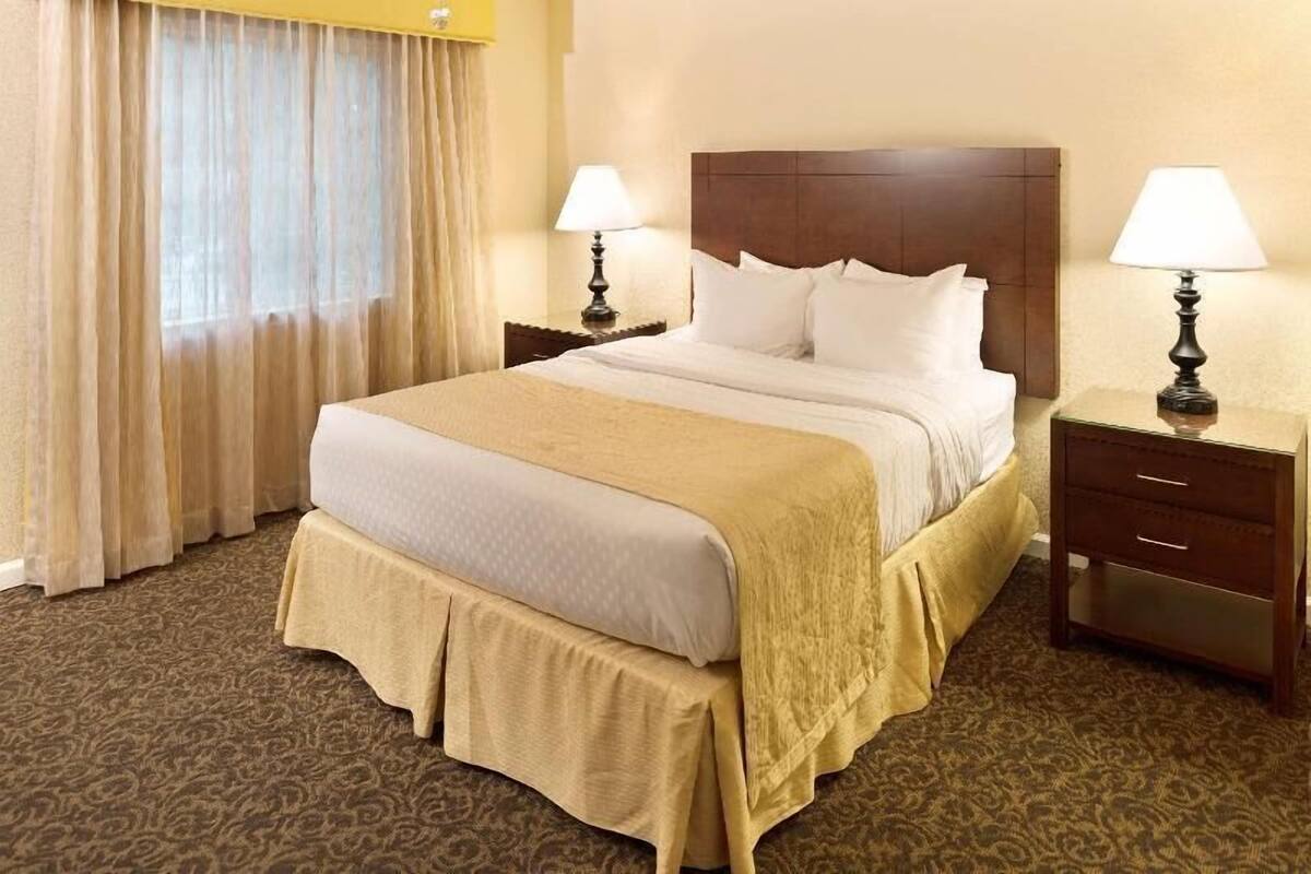 A hotel room with a large bed, two bedside tables, a window with curtains, and a carpeted floor.