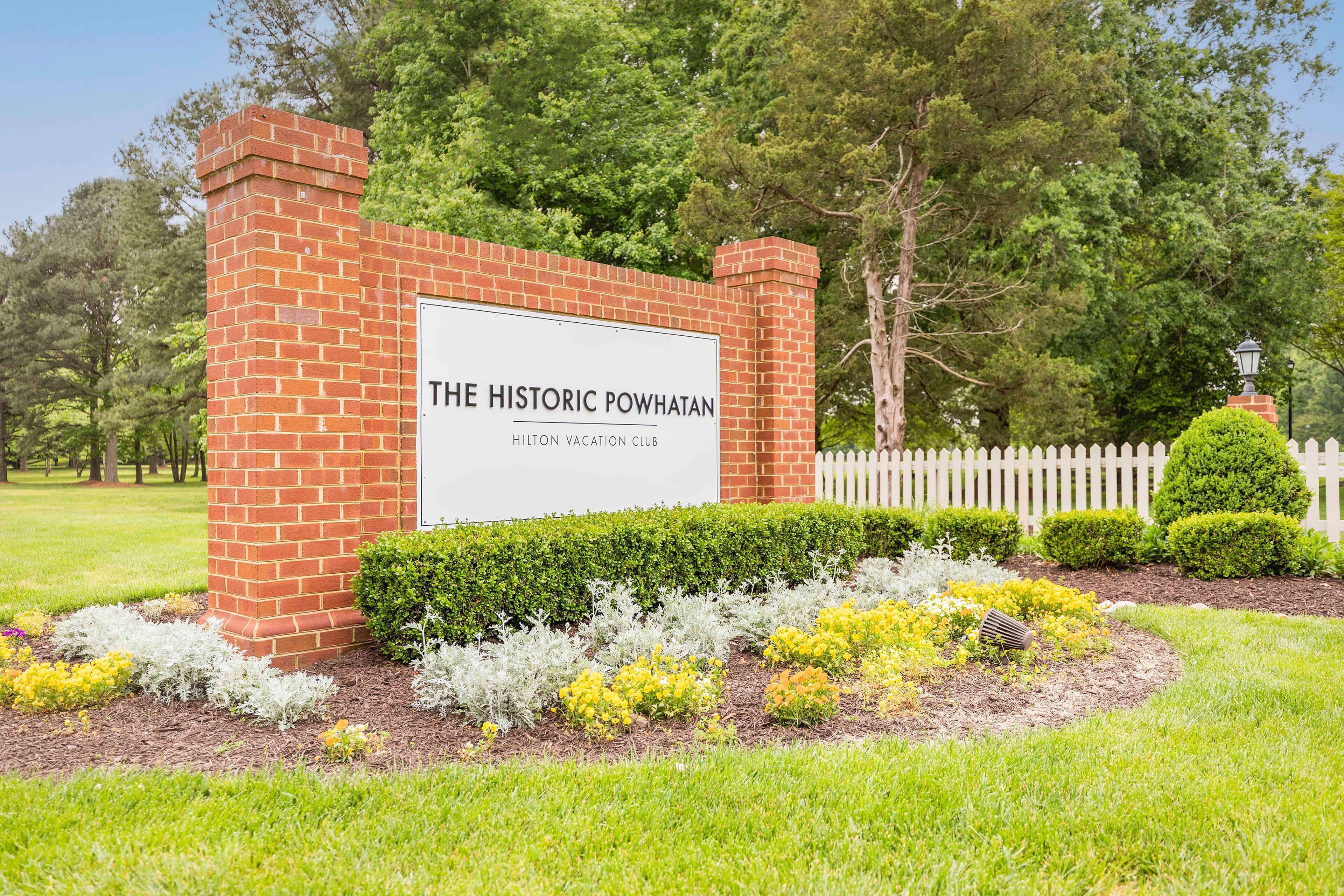 A brick sign with the text "The Historic Powhatan Hilton Vacation Club" surrounded by landscaped garden beds and a white picket fence.