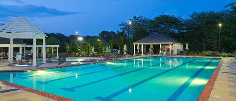 A swimming pool with clear blue water, surrounded by a brick deck and a gazebo.