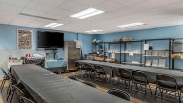 A conference room with tables and chairs, a television, and shelves with various items.