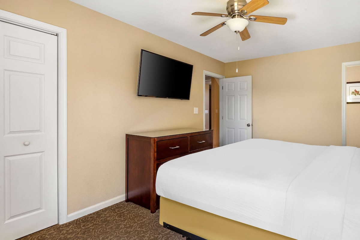 Quarto com cama, penteadeira, televisão e ventilador de teto.