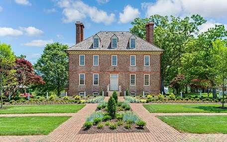 A large brick building with a central entrance, surrounded by well-maintained gardens and trees.
