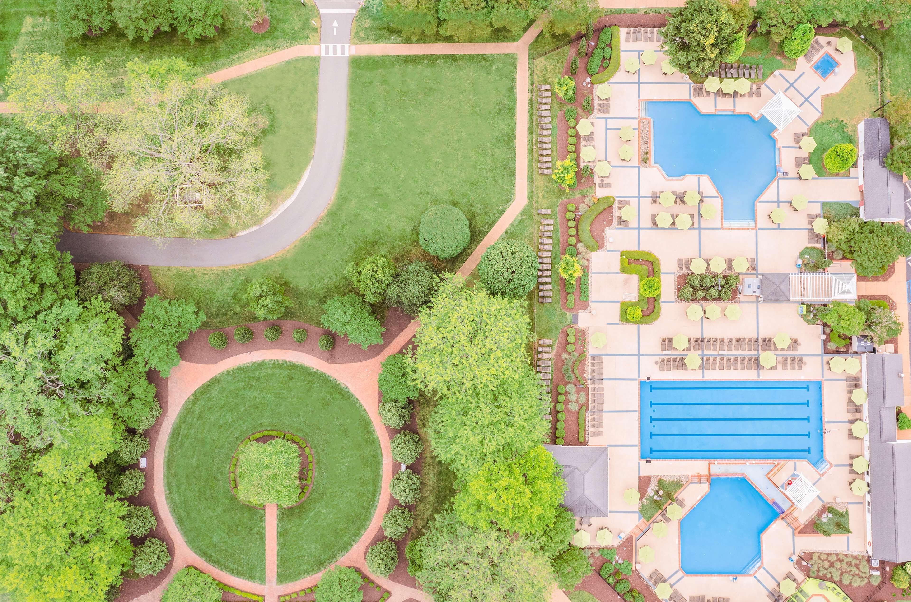 Vue aérienne d’un hôtel doté d’une piscine centrale, de jardins aménagés et d’une route sinueuse.