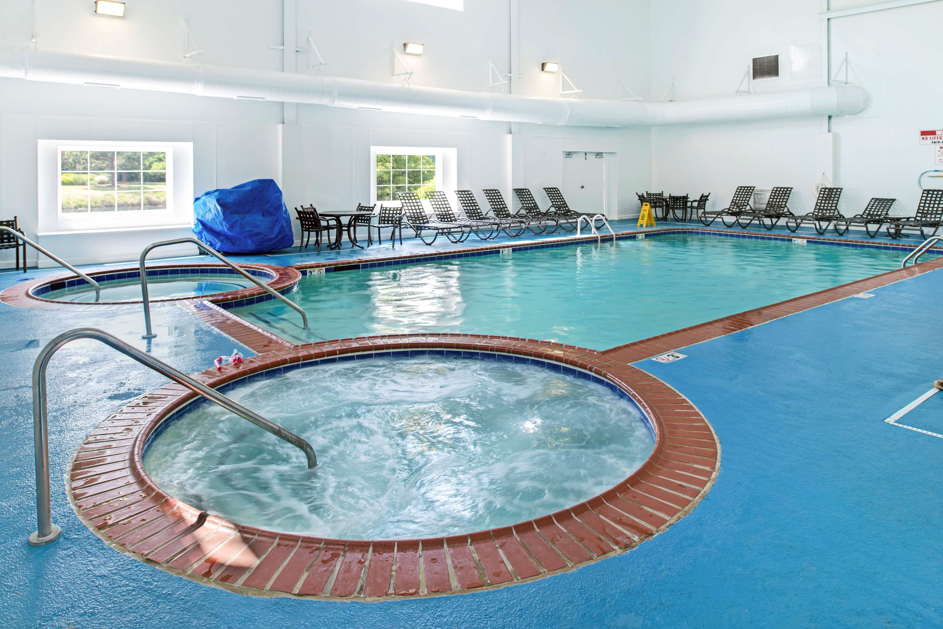 Una piscina interior con hidromasaje, sillas de descanso y una zona de estar cubierta.