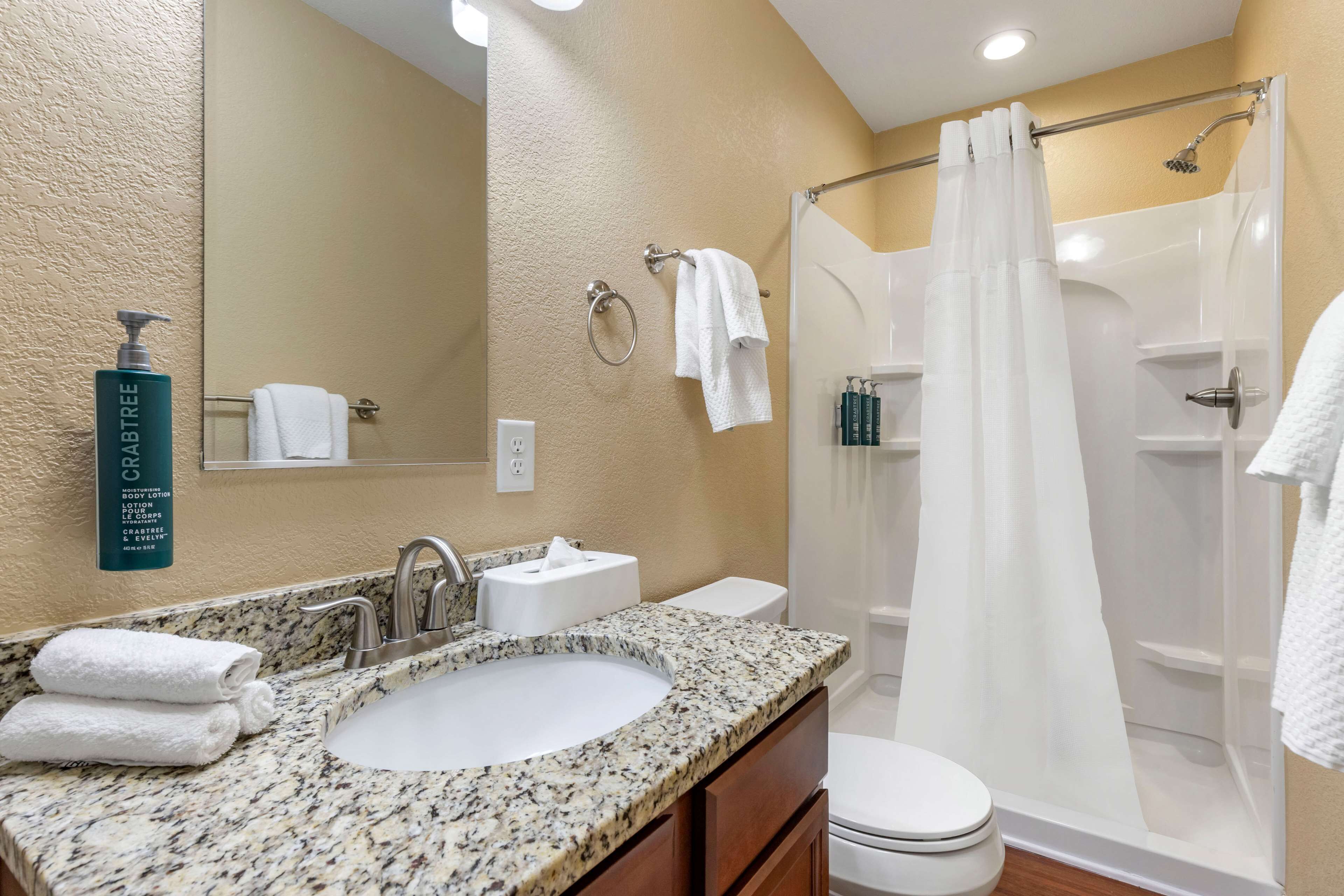 A bathroom with a granite countertop sink, a mirror, a toilet, and a shower with a curtain.