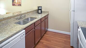 A kitchen with granite countertops, stainless steel sink, wooden cabinets, a coffee maker, and a refrigerator.