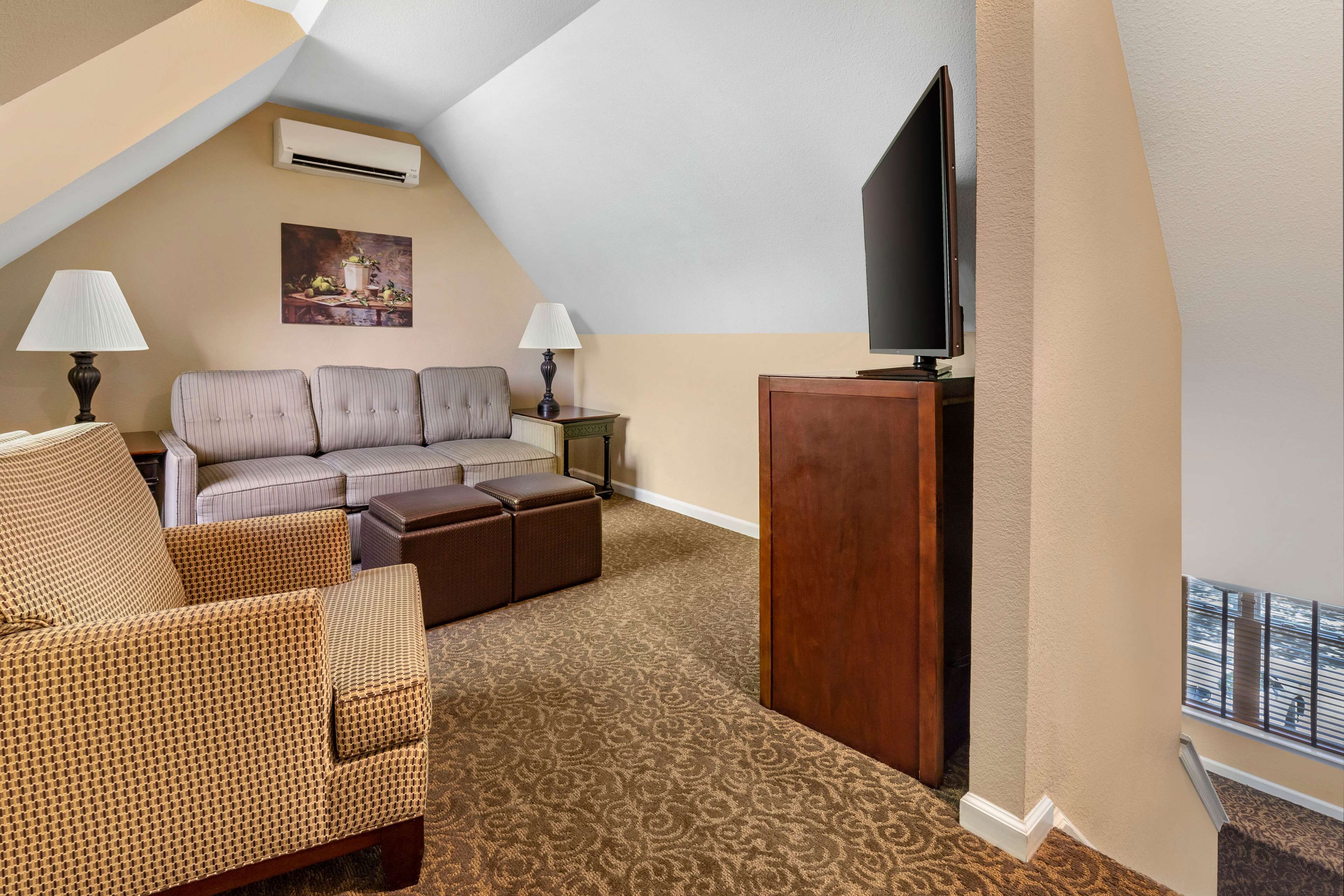 Habitación de hotel con sofá, reposapiés y un televisor de pantalla plana sobre un soporte de madera.