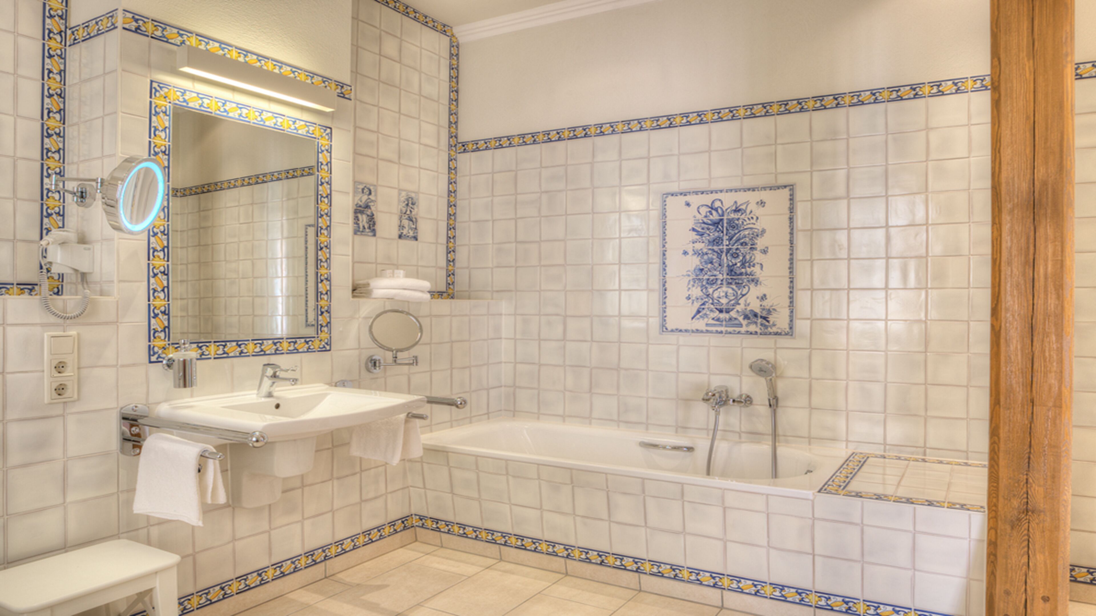 A bathroom with a sink, mirror, and bathtub, featuring decorative tiles and a wooden door frame.