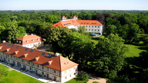 Ein großes Gebäude mit rotem Dach, umgeben von üppiger Vegetation und Bäumen.