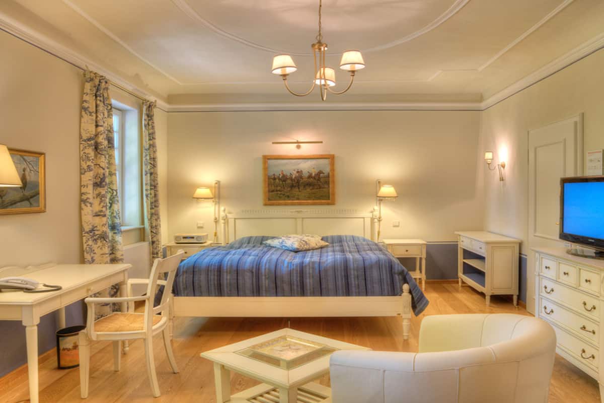 Una habitación de hotel con cama, escritorio, silla, televisión y un cuadro en la pared.