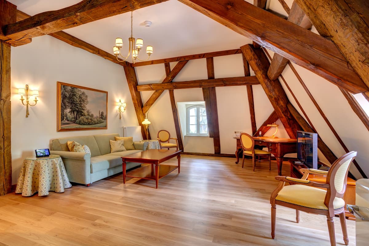 Habitación estilo loft con vigas de madera a la vista, suelo de madera, sofá, mesa de centro y escritorio con silla.