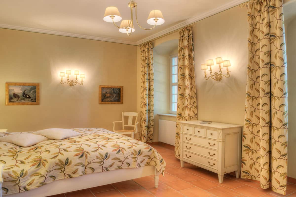 Un dormitorio con cama, cómoda, dos apliques de pared y una ventana con cortinas.