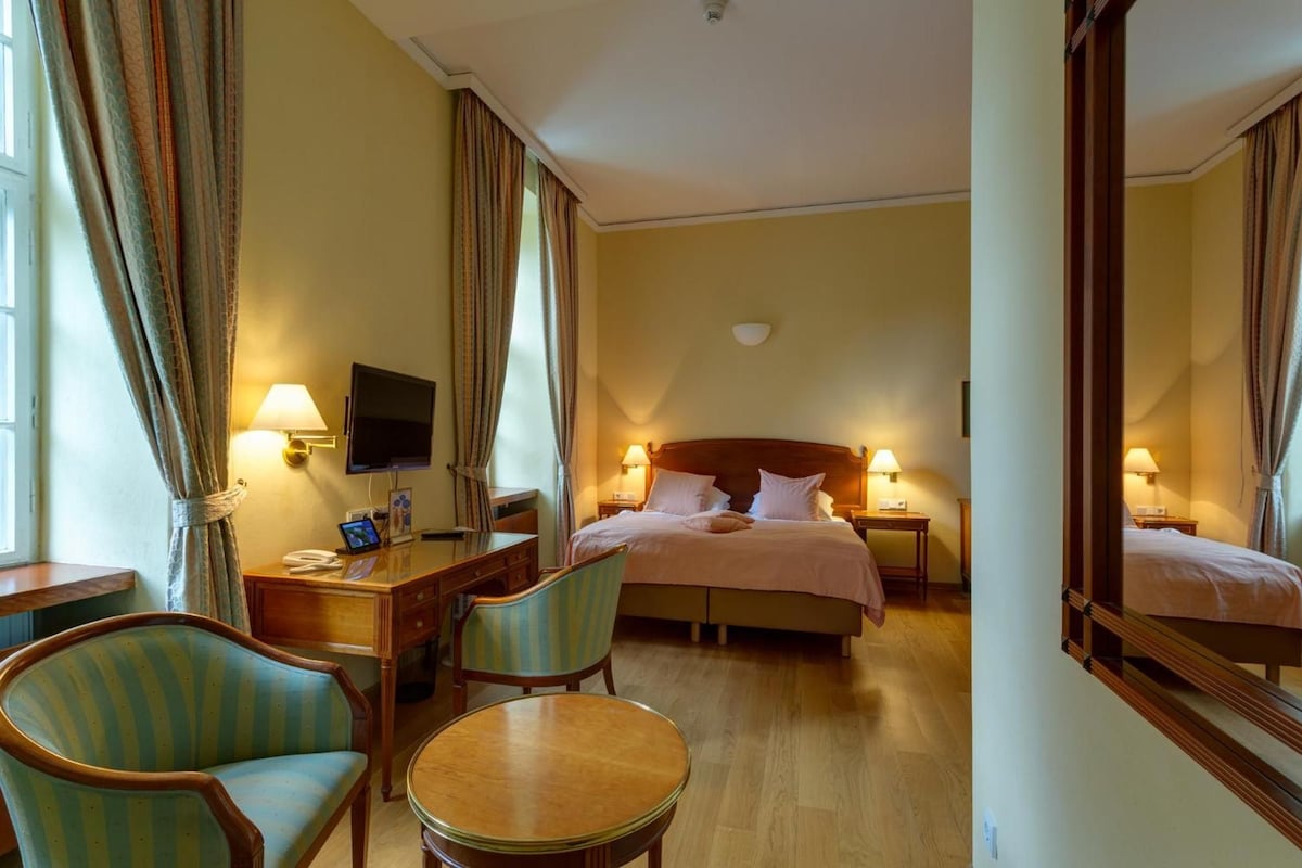 Une chambre d’hôtel comprenant un lit, des tables de chevet, un bureau avec une chaise, une télévision et un miroir.