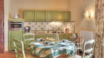 Une cuisine avec des meubles de couleur verte, une table à manger dressée pour quatre personnes et une machine à café.