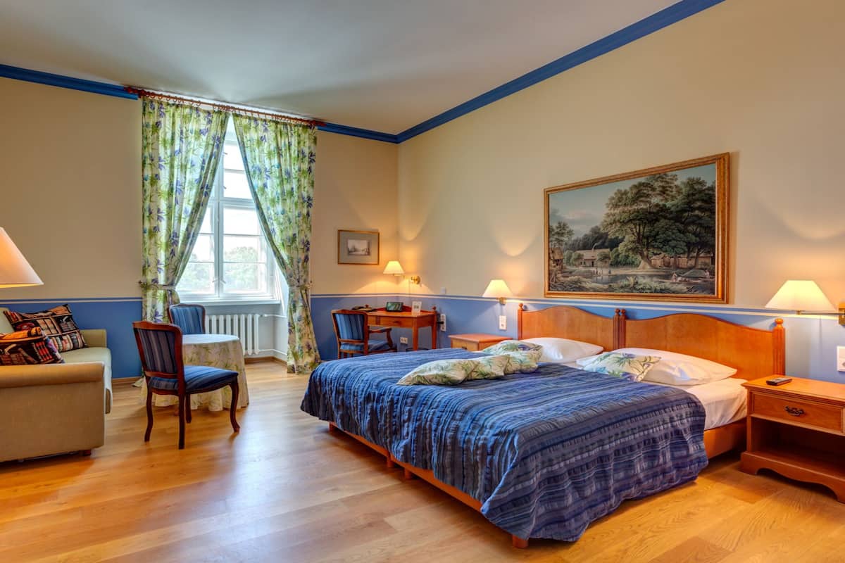 Habitación de hotel con cama, escritorio, silla, sofá y ventana con cortinas.