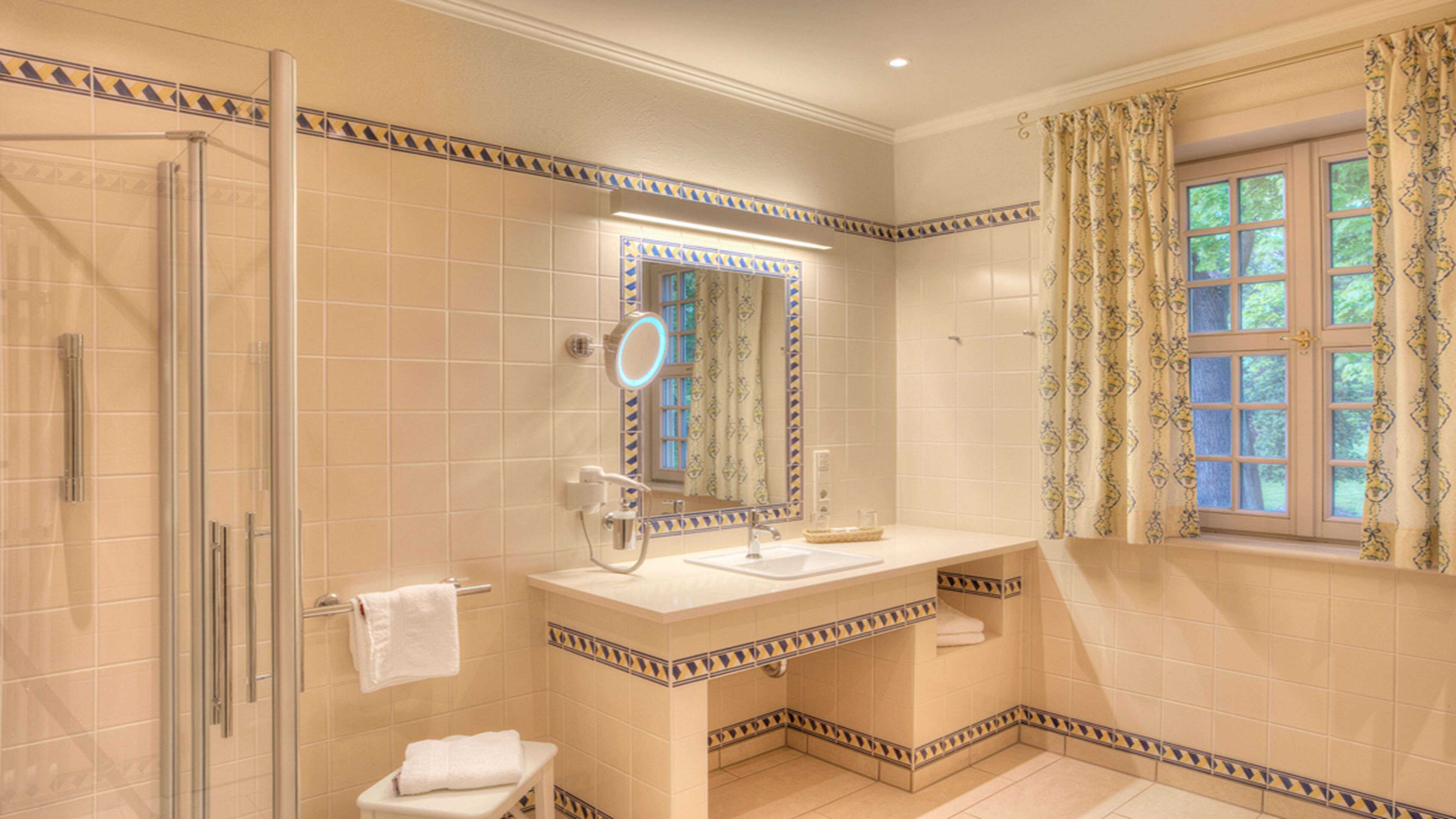 A bathroom with a glass shower enclosure, a sink with a mirror, and a window with curtains.